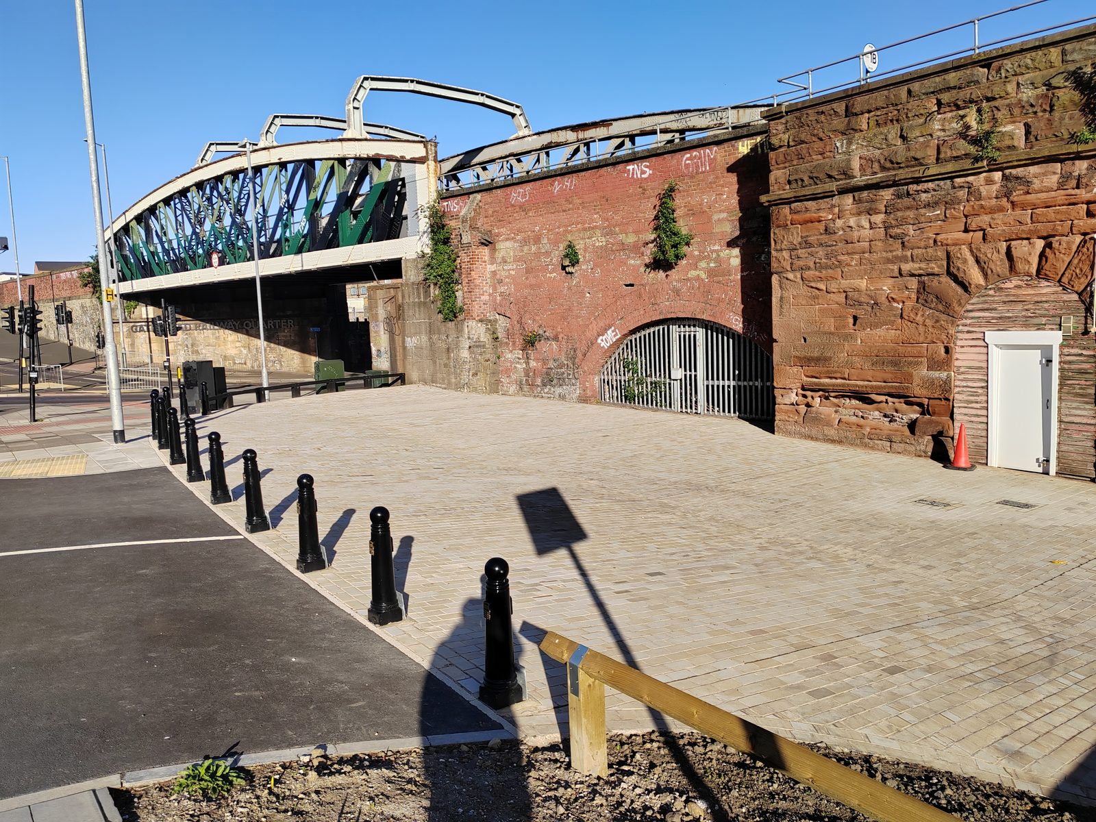 The open plot at the west end of the Askew Road arches, showing the bridge ramp above, a gated arch, and the paved area where the skatepark would be built.