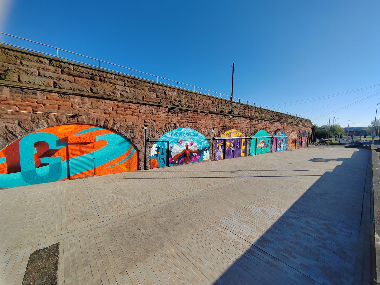 Perspective view along the full run of seven railway arches from the west end, with colourful murals on each arch receding into the distance.